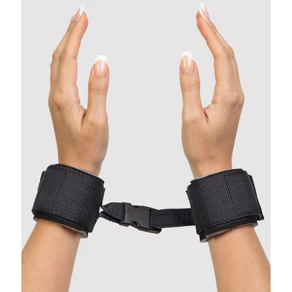 Adjustable wrist restraint cuffs connected with a quick-release buckle and soft padded lining.