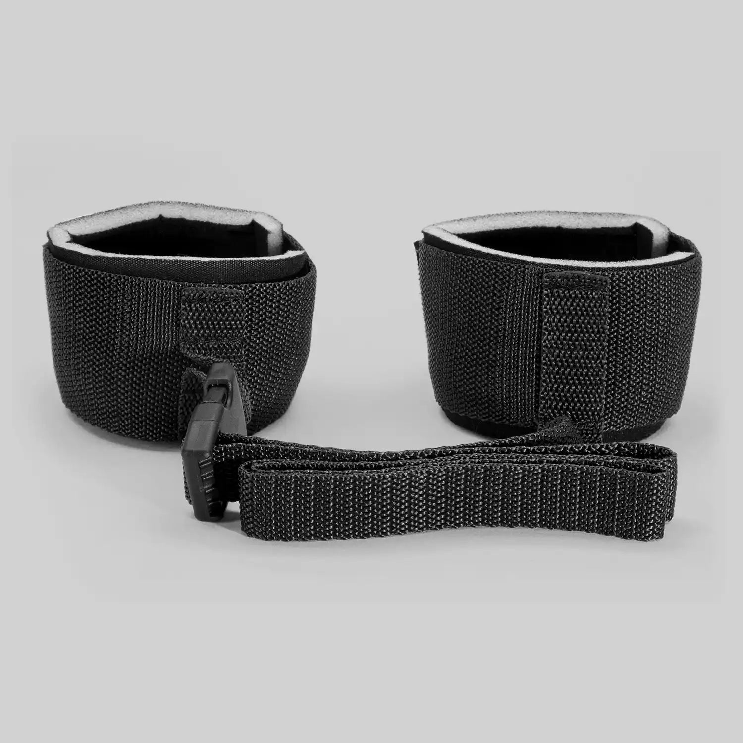 Adjustable wrist restraint cuffs connected with a quick-release buckle and soft padded lining.