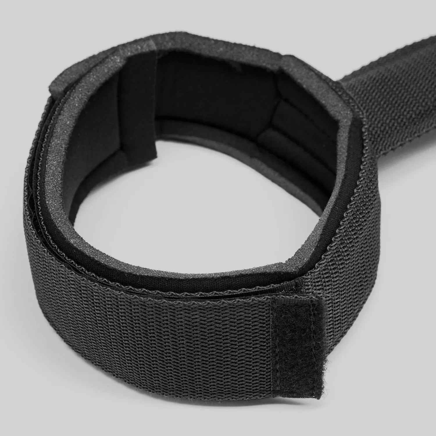 Black adjustable thigh restraint strap with flexible connector and padded leg cuffs.