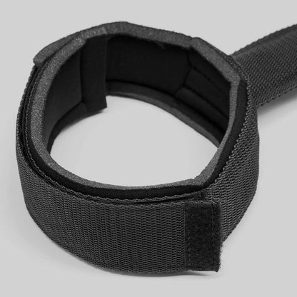 Black adjustable thigh restraint strap with flexible connector and padded leg cuffs.
